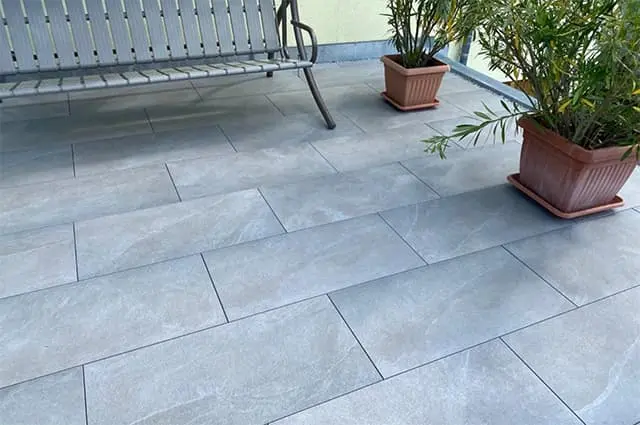 Teilansicht der neu gefliesten Terrasse mit Bank und Pflanzkübeln
