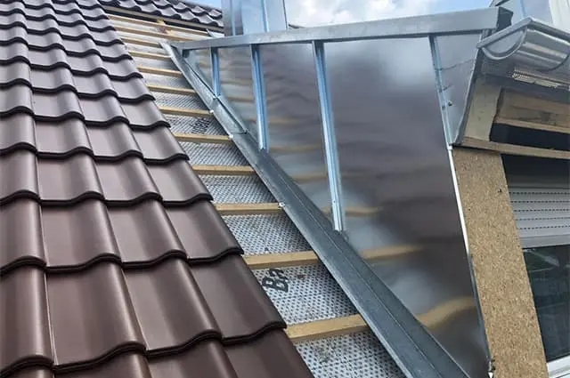 Neue Blechverkleidung aus hellem Metall an einem Giebel mit Ziegelanschluss