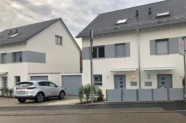 Zwei moderne weiße Neubauten mit grauem Dach und Sancolor-Fahrzeug davor