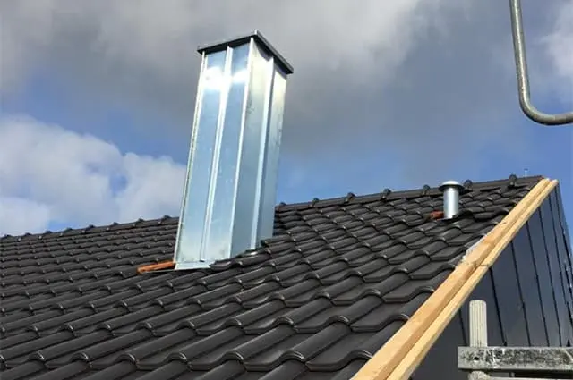 Neu verkleideter Kamin aus Metall auf dunkel gedecktem Dach