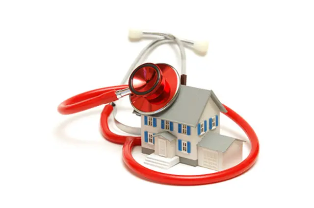 Stethoskop liegt um ein Modellhaus – symbolisiert Gebäudediagnose